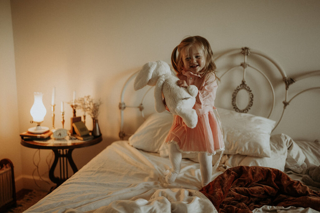 little girl jumping on the bed with her stuffed animals | nostalgic motherhood photoshoot